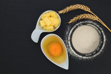 Food concept  base of bakery ingredients flour, egg and butter on black slate stone plate