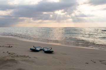 Fototapeta na wymiar beach slippers on the sand at sunset and sea