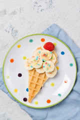 Sweet waffle with banana and strawberry in a shape of ice cream cone, meal for kids idea, top view