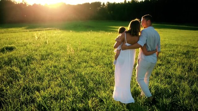 Happy family. Dad mom and a little girl, walking in a field dressed in white under the rays of the setting sun
