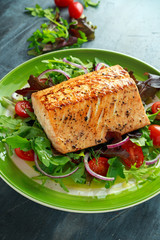 Baked salmon steak with tomato, onion, mix of green leaves salad in a plate. healthy food