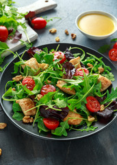 Fresh salad with chicken breast, arugula, nuts and tomatoes on black plate in a wooden table.