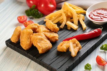 Tasty nuggets, french fries and small bowl with sauce for chicken on wooden board