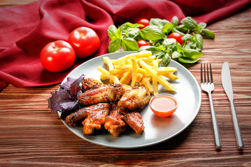Tasty chicken wings, french fries and small bowl with sauce on wooden table