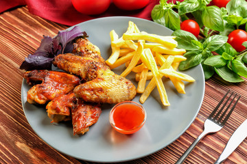 Tasty chicken wings, french fries and small bowl with sauce on wooden table
