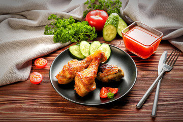 Tasty chicken legs and small bowl with sauce on wooden table