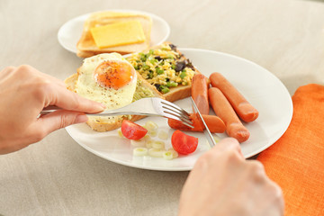 Woman eating tasty fried egg, sausages and toasts on table in kitchen. Cooking for one concept