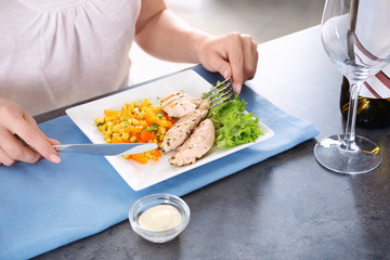 Woman eating tasty chicken meat with vegetables on table in kitchen. Cooking for one concept