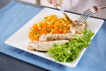 Woman eating tasty chicken meat with vegetables on table in kitchen. Cooking for one concept
