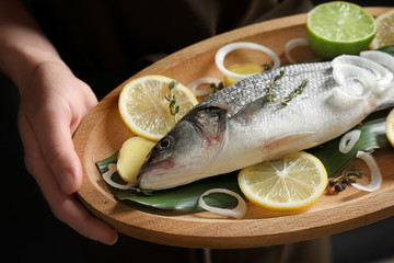Woman holding wooden dish with fresh fish, closeup