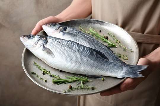 Woman holding metal dish with fresh fish in hands
