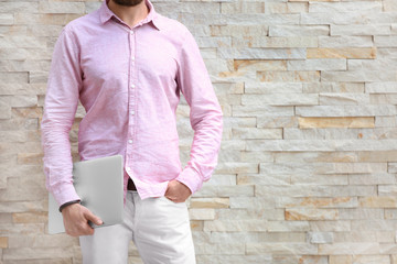 Young blogger with laptop near brick wall