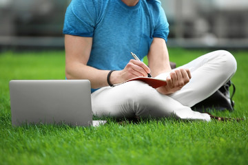Naklejka premium Young blogger with laptop sitting on green grass, outdoors