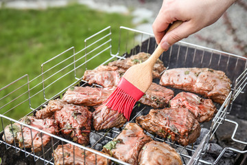 Man spreading sauce on ribs with brush outdoors