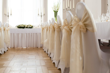 Fototapeta na wymiar Close-up photo of back of chairs decorated with white cloth cover and big cream satin ribbon tied to a bow