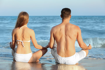 Young couple practicing yoga on sea beach