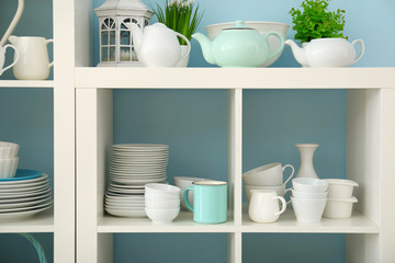 White storage stand with ceramic dishware on color background