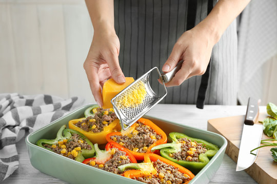 Woman adding cheese to quinoa stuffed peppers in kitchen