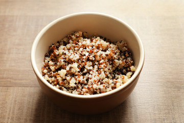 Bowl with boiled quinoa grains on wooden table