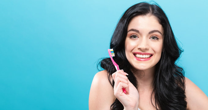 Young woman holding a toothbrush on a solid background