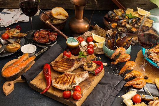 Overhead Of Dinner Table. Assorted Grilled Barbecue Meat And Seafood With Vegetable. Pork Grilled Steaks, Baked Mussels, Shrimps, Cherry Tomato, Chili Pepper, Glass Of Wine. Picnic Bbq Party Concept.