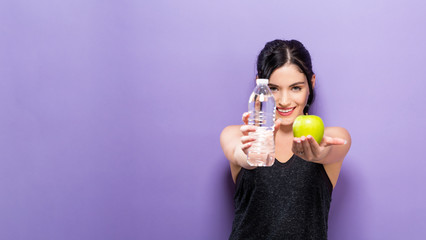 Happy young woman holding an apple and a water bottle