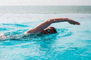 Woman swimming crawl in a pool with sea view