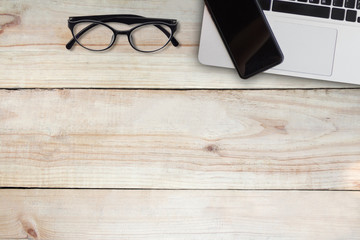 Eyeglasses and mobile phone over laptop on wooden table. top angle view. copy space