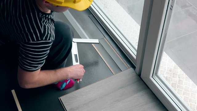 worker with pencil make markings on laminate floor board