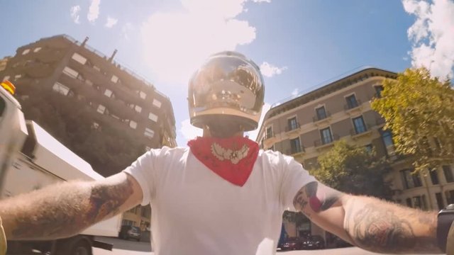 Cool and confident stylish motorcyclist in bandana and white tshirt explores streets of Barcelona on vintage retro cafe racer motorcycle, streets and buildings sweep around him