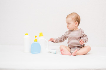beautiful baby holding a bottle in the hand with shower gel, beside lies Baby cosmetic tubes on white isolated background