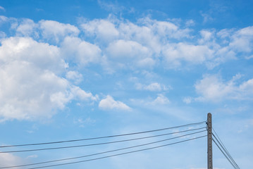 Fluffy soft white clouds with blue sky in day time light and electric pole in bottom.
