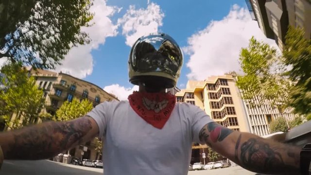Cool confident hipster brutal man with arm tattoos sleeves rides motorbike in vintage retro protective helmet with bubble mirrored visor, in middle of busy city with traffic around him