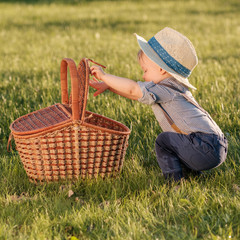 Toddler child outdoors. One year old baby boy wearing straw hat looking in picnic basket