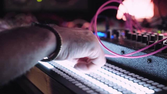 Close focus on musician hand is pressing buttons and keys on his midi mix keyboard with blinking leds. Professional sound producer at work in dark room of his studio.