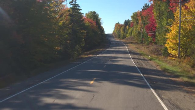 POV: Driving on empty road through stunning colorful forest on sunny autumn day. FPV People on leaf peeping road trip driving through autumn forest in sunny fall. Beautiful fall foliage nature drive