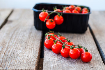 A branch of red organic cherry tomatoes on a wooden background