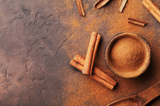 Heap of cinnamon sticks and powder on brown rustic background top view. Aromatic spices.