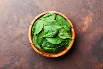 Green baby spinach leaves in wooden bowl on rustic stone table top view. Organic healthy food.