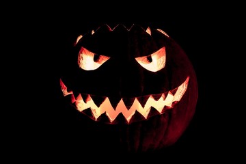 Round halloween pumpkin smile with hot burning fire eyes mouth. The big helloween symbol has a mad face glowing eyes and also a glow in its mouth and teeth. Black orange nightmare of October 31st