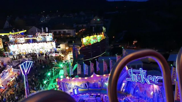 Blick vom Riesenrad auf einen bunt beleuchteten Festplatz. 