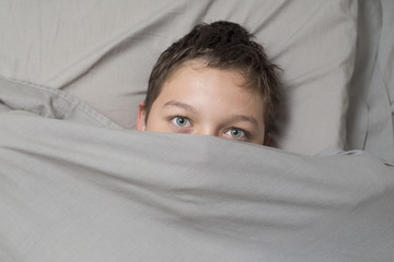 Top view of teenage girl in bed covering her face with blanket. child with fear.