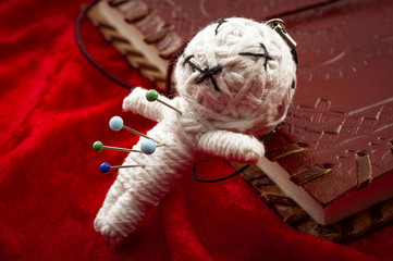 Witchcraft and place a jinx or put a spell on someone concept with a voodoo doll pierced by needles to cause harm to a victim leaning on a book of spells. Each needle represents a different curse
