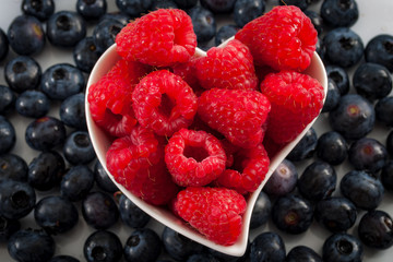 Fresh berry fruits and healthy eating concept with mixed blueberries and raspberries in a heart shaped bowl