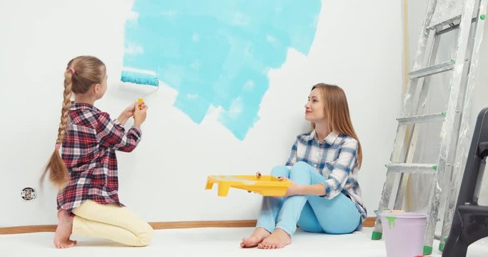 Cheerful mother and daughter painting wall at home