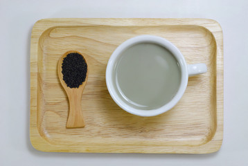 Water the Back Sesame in a white cup and Back Sesame in a wood spoon on wood plate.