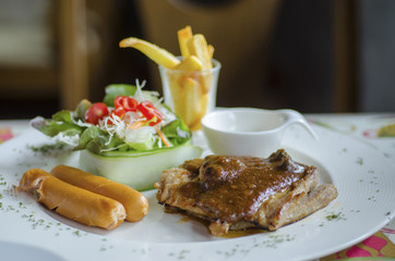 Pork steak is placed in a dish with fried potatoes, salads and pork sausage.
