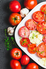 Tomato slices in a baking dish with garlic and thyme. Top view, space for text.