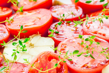 Tomato slices in a baking dish with garlic and thyme. Selective focus, close up.