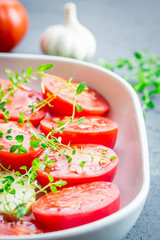 Tomato slices in a baking dish with garlic and thyme. Close up.